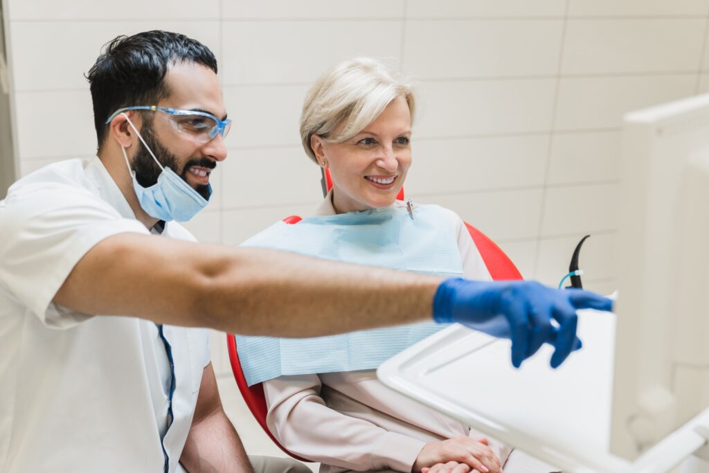 Orthodontist showing explaining x-ray photo of jaws on computer screen to patient in dental clinic