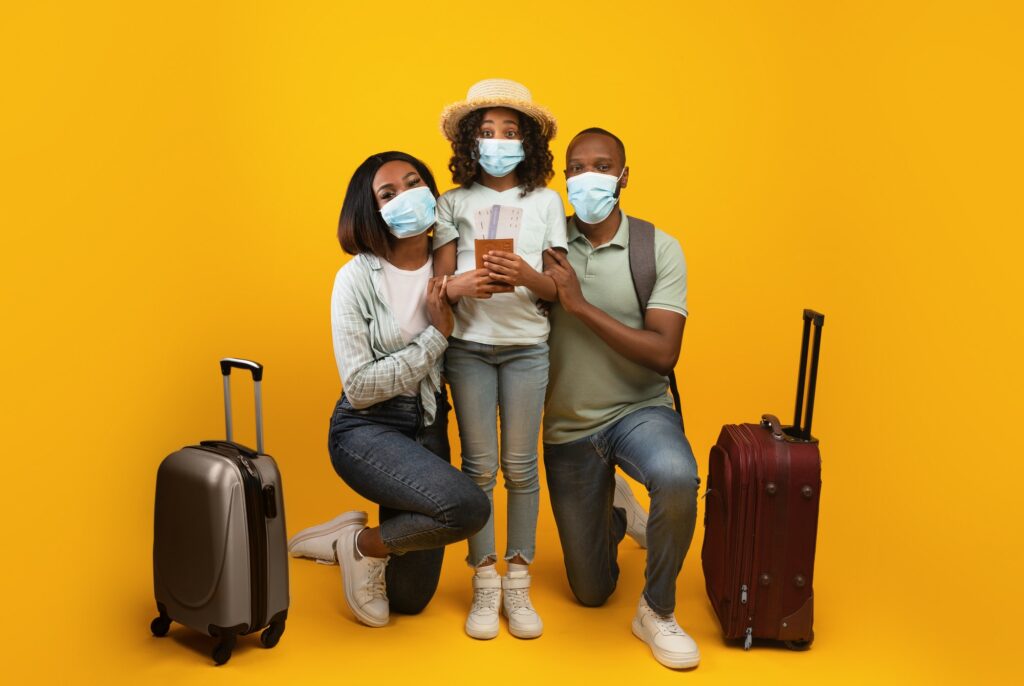 Safe travels. African american family wearing medical masks, posing with suitcases and passports